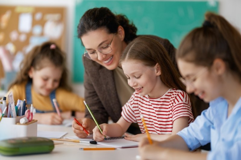 Happy kids and teacher at school. Woman and children are working in the class.