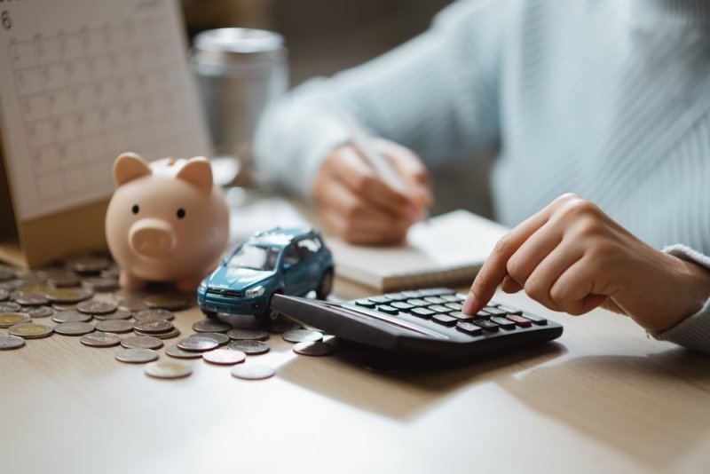 a person calculating insurance policy cost with a piggy bank and car model on the table