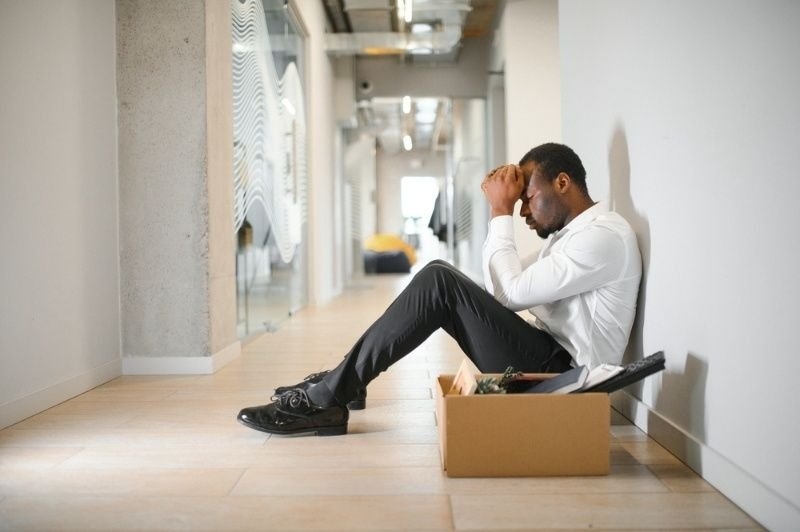 Upset man sitting beside a box of belongings after losing his job.