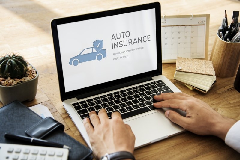 A person uses a laptop displaying an “AUTO INSURANCE” graphic with a car and shield icon.