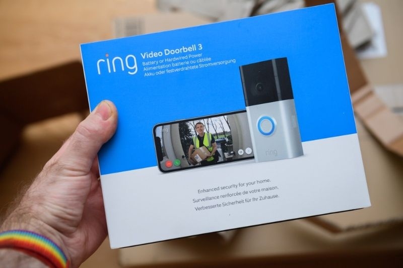 Person holding a Ring Video Doorbell 3 product box with smart doorbell and mobile app display.