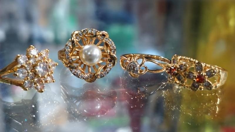 Three vintage-style gold rings featuring diamonds, pearls, and colorful gemstones displayed on a jewelry showcase.