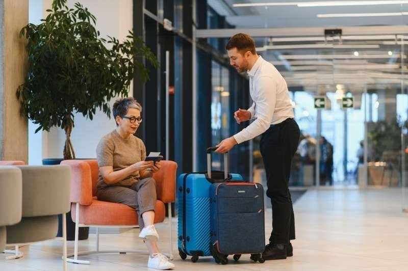 Airport staff assisting a seated traveler with luggage and travel documents in a modern terminal.