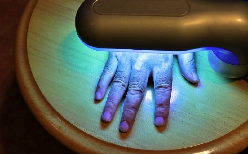 Hand placed under a UV nail lamp on a table, curing nail polish during a manicure.