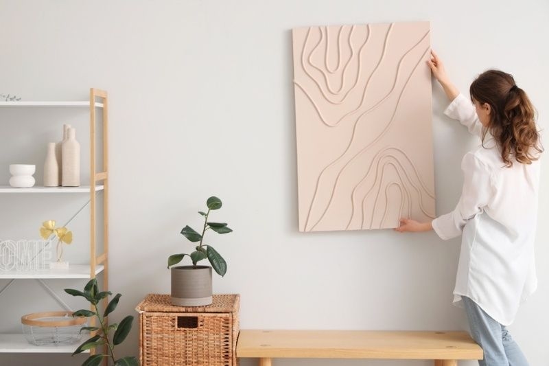 Woman hanging minimalist textured wall art in a modern living room.