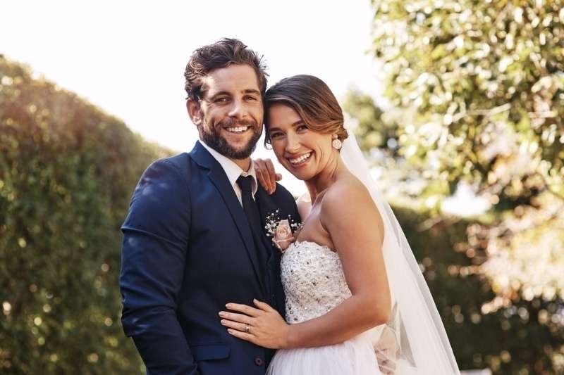 Smiling newlywed couple embracing outdoors in wedding attire.