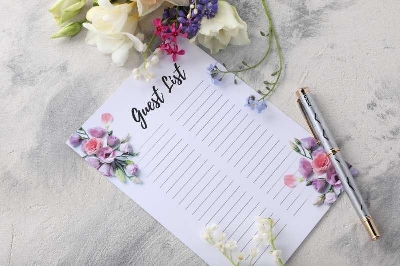 A decorative card labeled “Guest List” surrounded by colorful flowers and a pen.