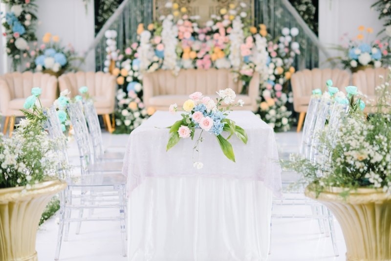 A beautifully decorated wedding venue featuring a charming floral arrangement, transparent chairs, and a white-draped table.
