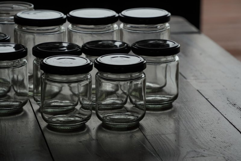 Several empty glass jars with black lids arranged on a rustic wooden table.