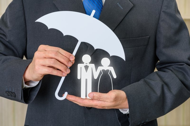 Business professional holding a white umbrella-shaped symbol protecting a paper cutout of a bride and groom.