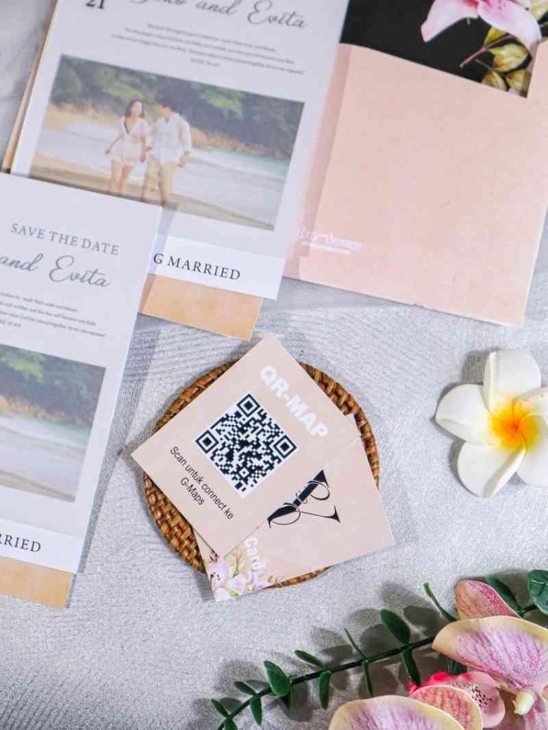 Close-up of wedding invitation stationery featuring a QR code card, floral envelope liner, and tropical flower decorations.
