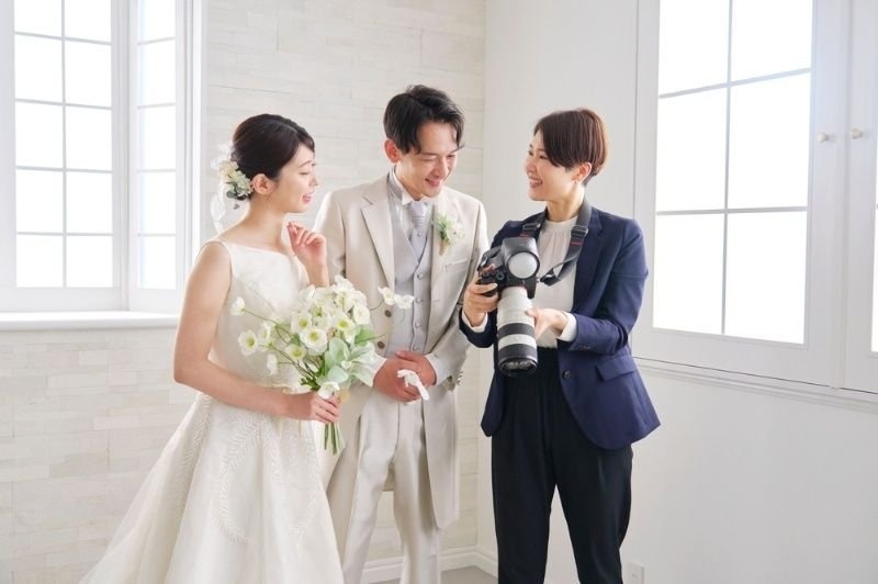 Wedding photographer reviewing captured wedding photos on a DSLR camera with the bride and groom, sharing images and discussing the results after the photoshoot.