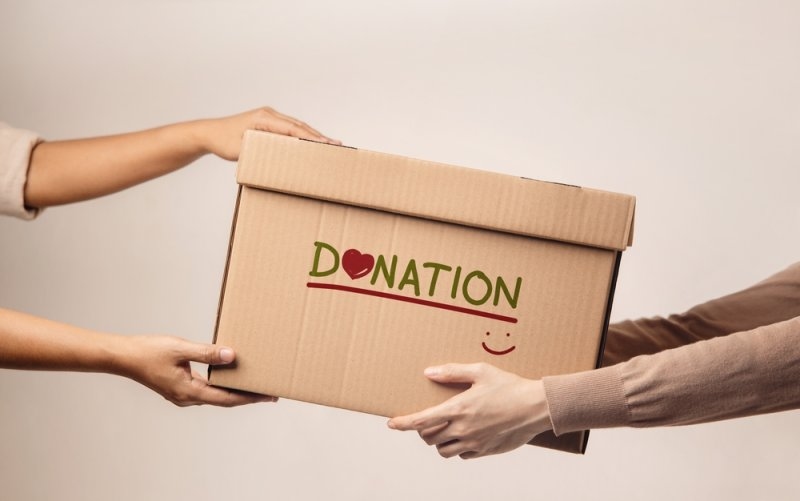 People exchanging a cardboard donation box labeled “DONATION.”