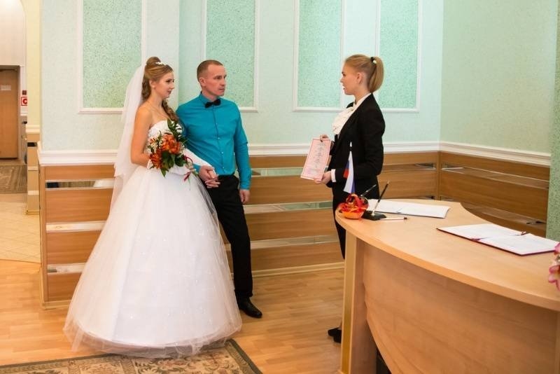 Bride and groom standing with a marriage registrar in a civil registration office during a wedding ceremony.