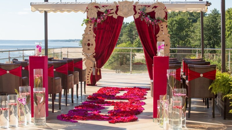 Outdoor wedding ceremony setup with red drapery, floral decorations, and a rose-petal aisle overlooking the water.