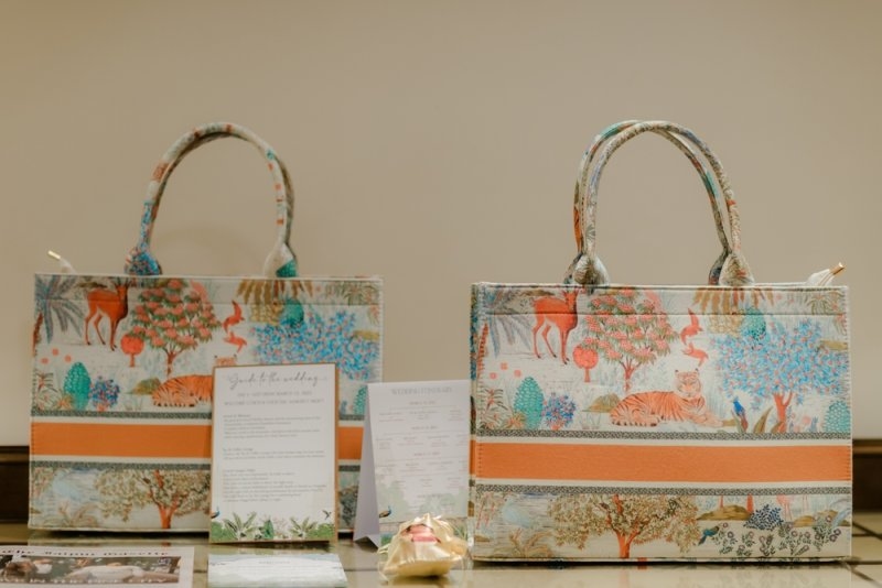 Two decorative floral-patterned wedding welcome bags displayed with stationery, informational cards, and a small gift.