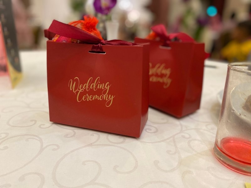 Red gift bags labeled “Wedding Ceremony” arranged on a decorated table.