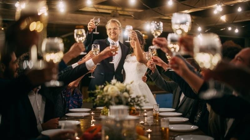Wedding guests raising glasses in a toast while the bride and groom celebrate at a reception.