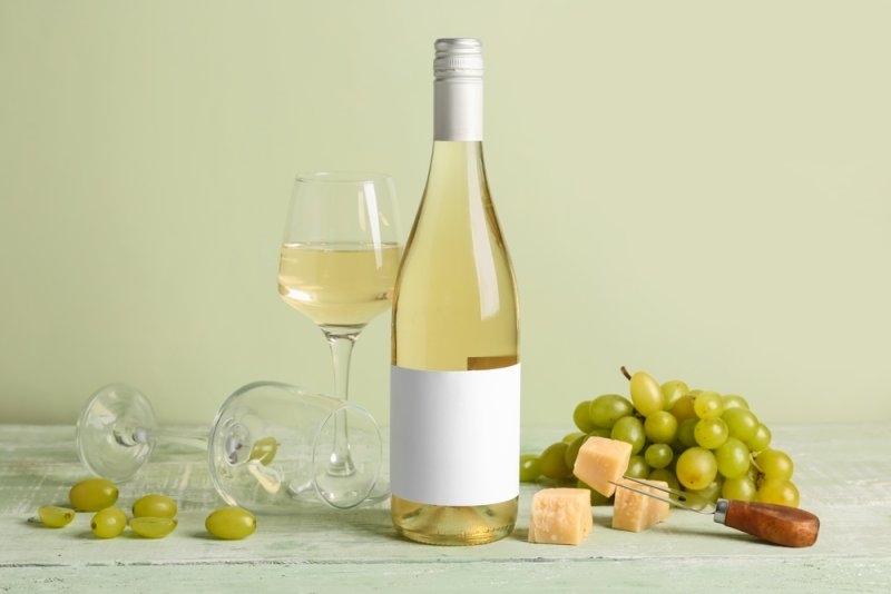 A bottle of white wine displayed with a filled wine glass, green grapes, and cheese cubes.