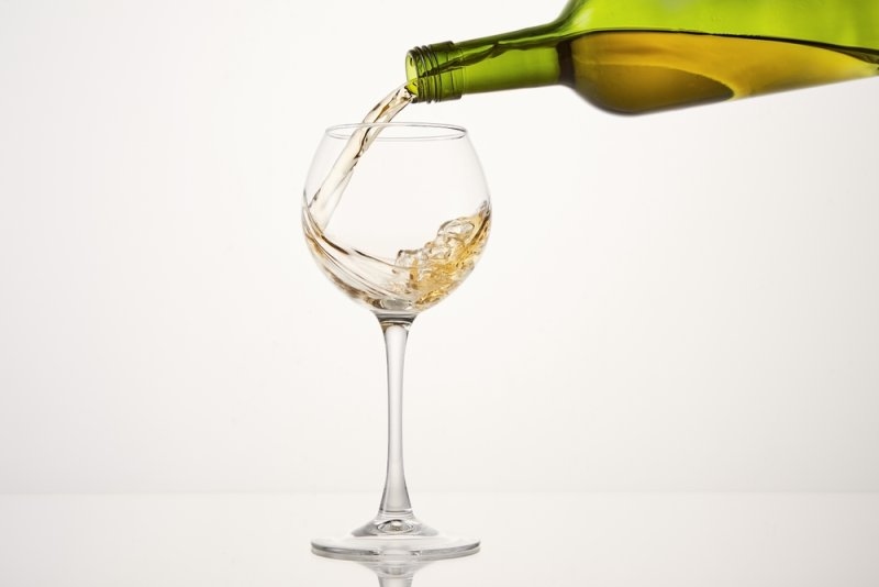 White wine being poured from a green bottle into an elegant wine glass against a clean white background.