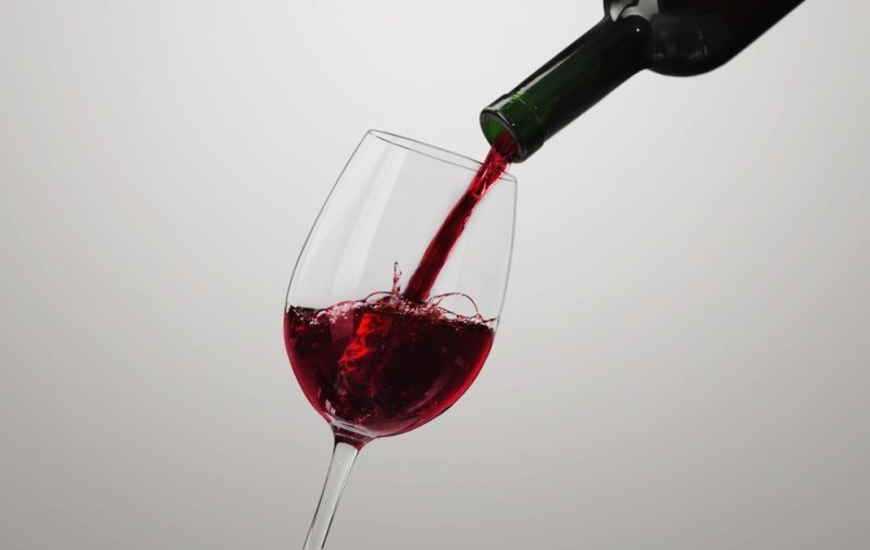 Red wine being poured into a clear wine glass from a bottle.
