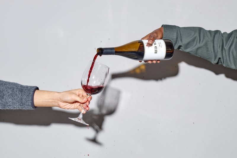 Person pouring red wine from a bottle into a wine glass.