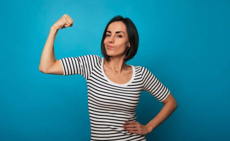 Confident woman in a striped shirt flexing her arm against a bright blue background.
