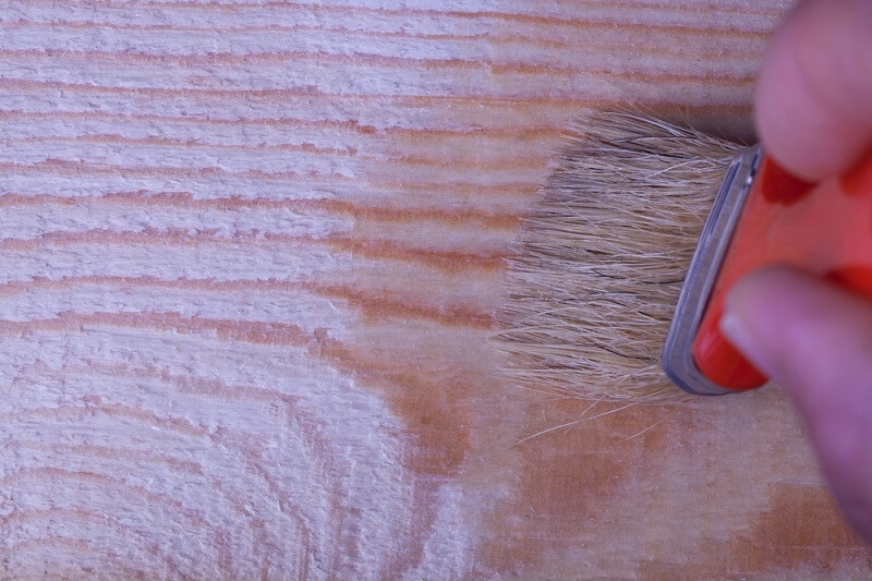 man brushing wooden furniture with oil brush