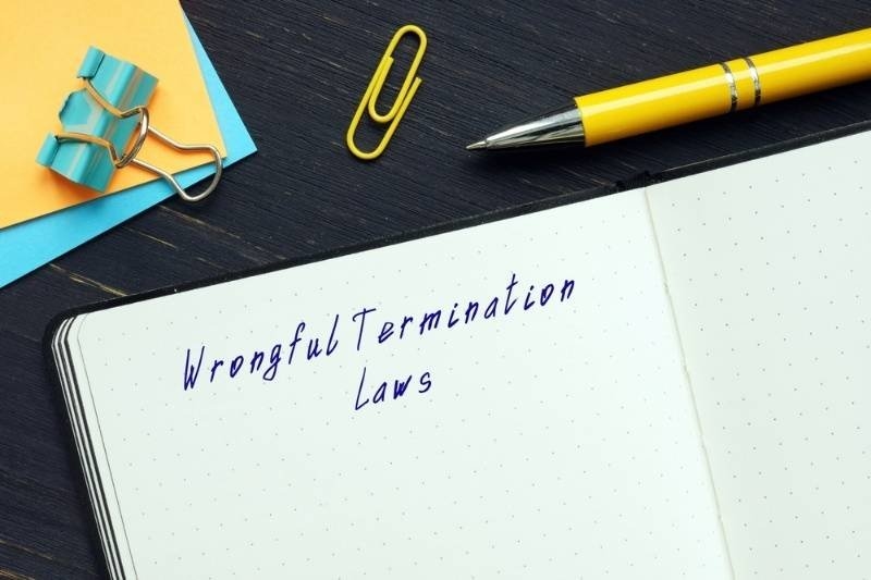 Notebook labeled wrongful termination laws with office supplies on desk.