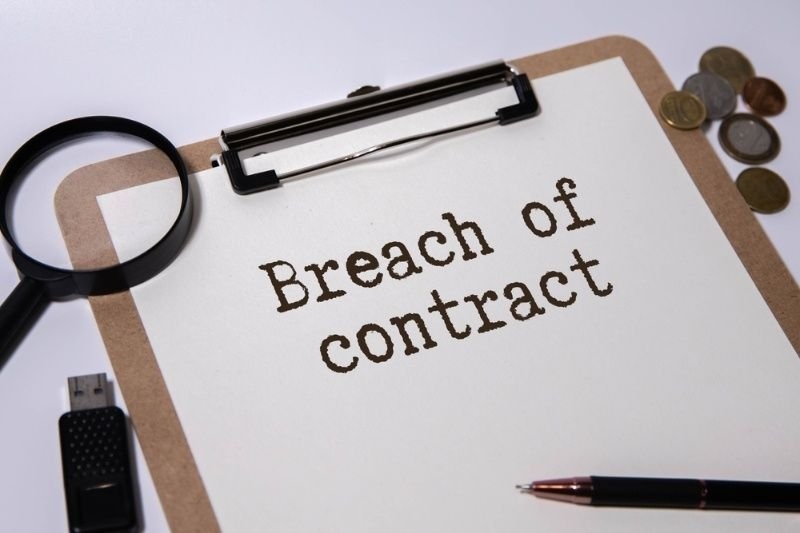 Clipboard displaying breach of contract document with magnifying glass and pen.